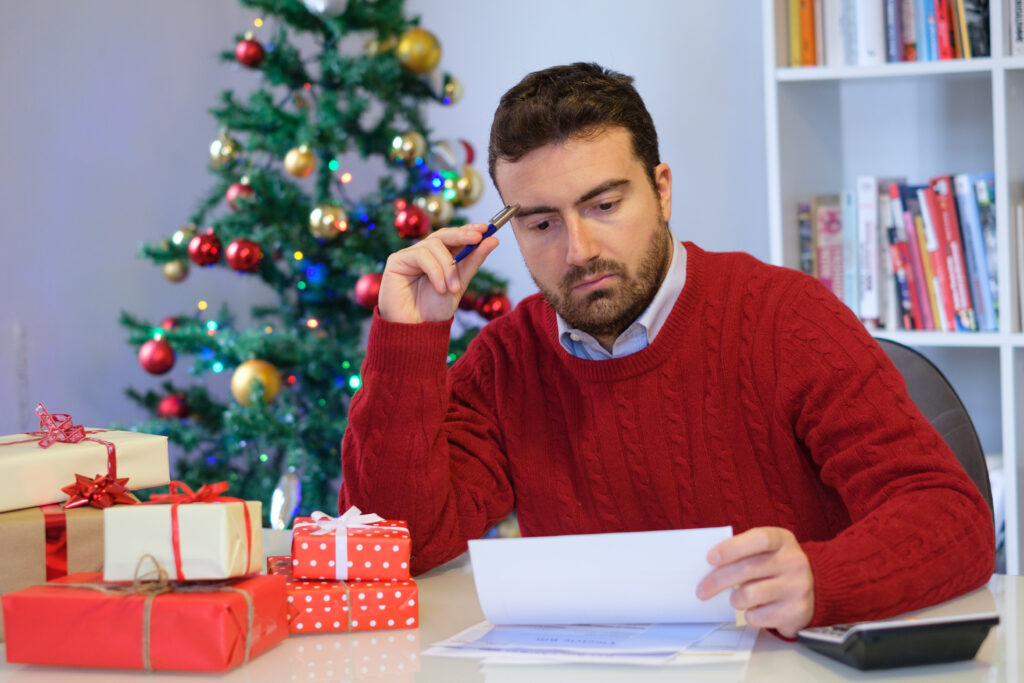 Man Upset Looking at Bills with Christmas Tree Man Upset Looking at Bills with Christmas Tree