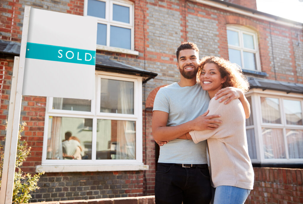 Happy Couple by Sold Real Estate Sign Happy Couple by Sold Real Estate Sign