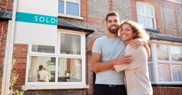 Happy Couple by Sold Real Estate Sign