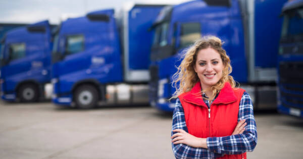 Female Trucker Smiling in Front of Trucks